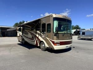 Brown and beige motorhome parked outdoors with blue sky and trees.
