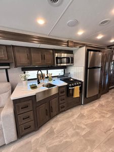 Modern RV kitchen with dark wood cabinets, stainless steel appliances, and white countertops.