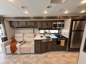 Modern RV kitchen with sofa and stainless steel appliances in 2023 Coachmen Mirada 35OS.