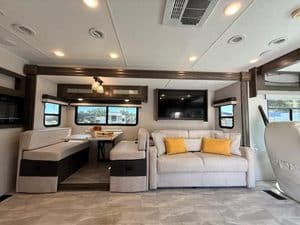Modern RV interior with sofa, dining area, and entertainment system.