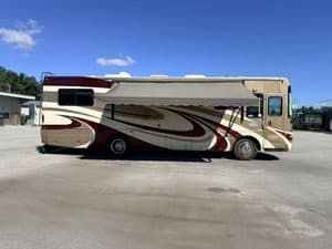 Large beige and maroon RV with slide-out for repairs at KA RV Repair.