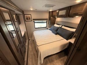 Cozy RV bedroom with large bed and wooden cabinets in 2023 Coachmen Mirada 35OS.