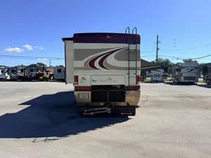 Rear view of a travel trailer in an RV repair lot with multiple RVs.