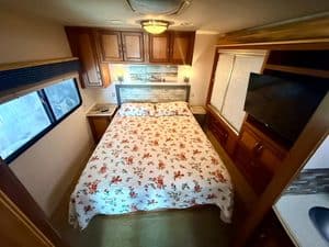 Comfortable RV bedroom with floral bedding, wooden cabinets, and a flat-screen TV.