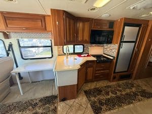 RV kitchen with wooden cabinets, microwave, refrigerator, and window view.
