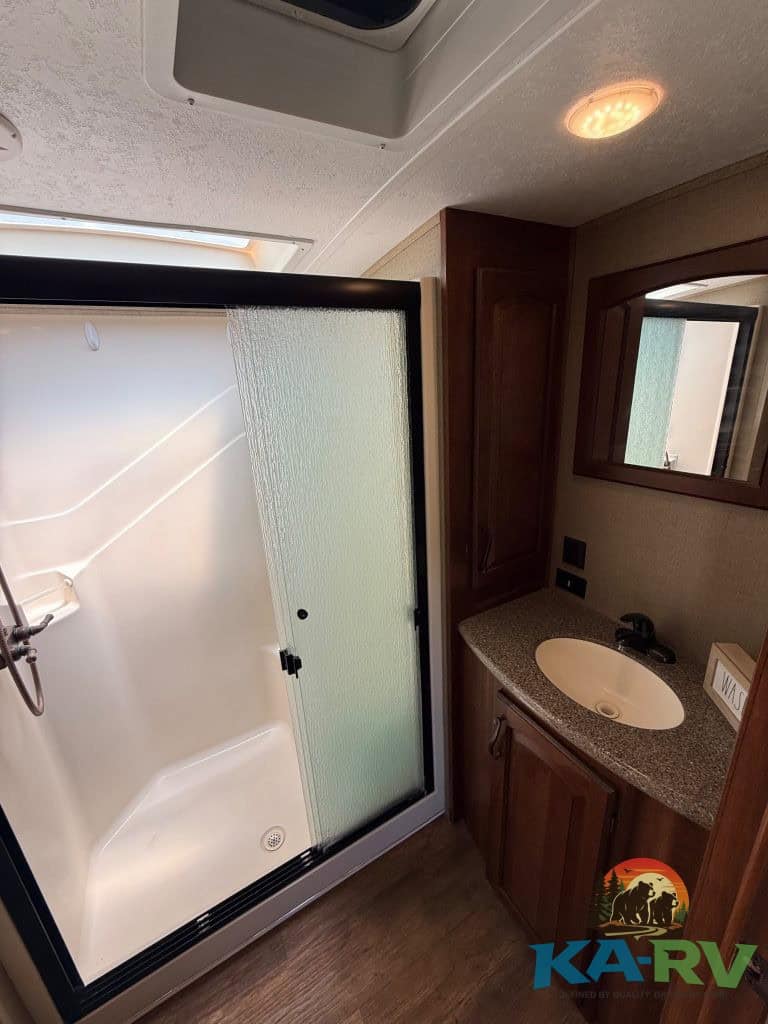 RV bathroom shower with frosted glass door and compact vanity with sink.