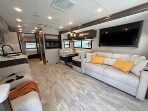 Spacious RV interior with sofa, TV, and kitchen area in 2023 Coachmen Mirada 35OS.