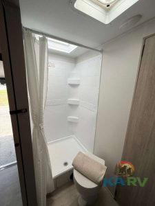 Small RV bathroom with shower, toilet, and storage shelves.