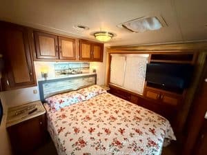Cozy RV bedroom with floral bedspread, wooden cabinets, and window blinds.