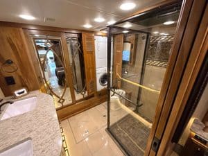 Luxury RV bathroom with shower, sink, and wooden cabinets.
