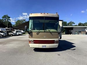 Front view of a beige and red RV bus at Tropical RV Repair shop.