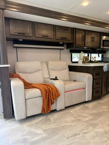 Comfortable RV sofa with orange throw blanket and kitchen in background.