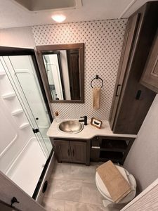 RV bathroom with shower, sink, mirror, and storage cabinets.