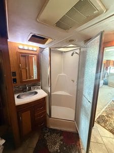 RV bathroom with shower, sink, and wooden cabinet mirror.