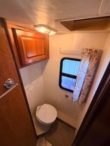 Small RV bathroom with toilet, window, and wooden cabinet.