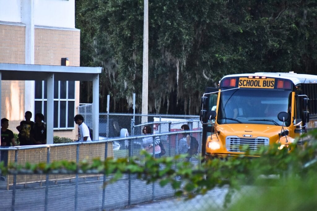 Students climb out of a school bus behind chain link fences at Buchholz High School.