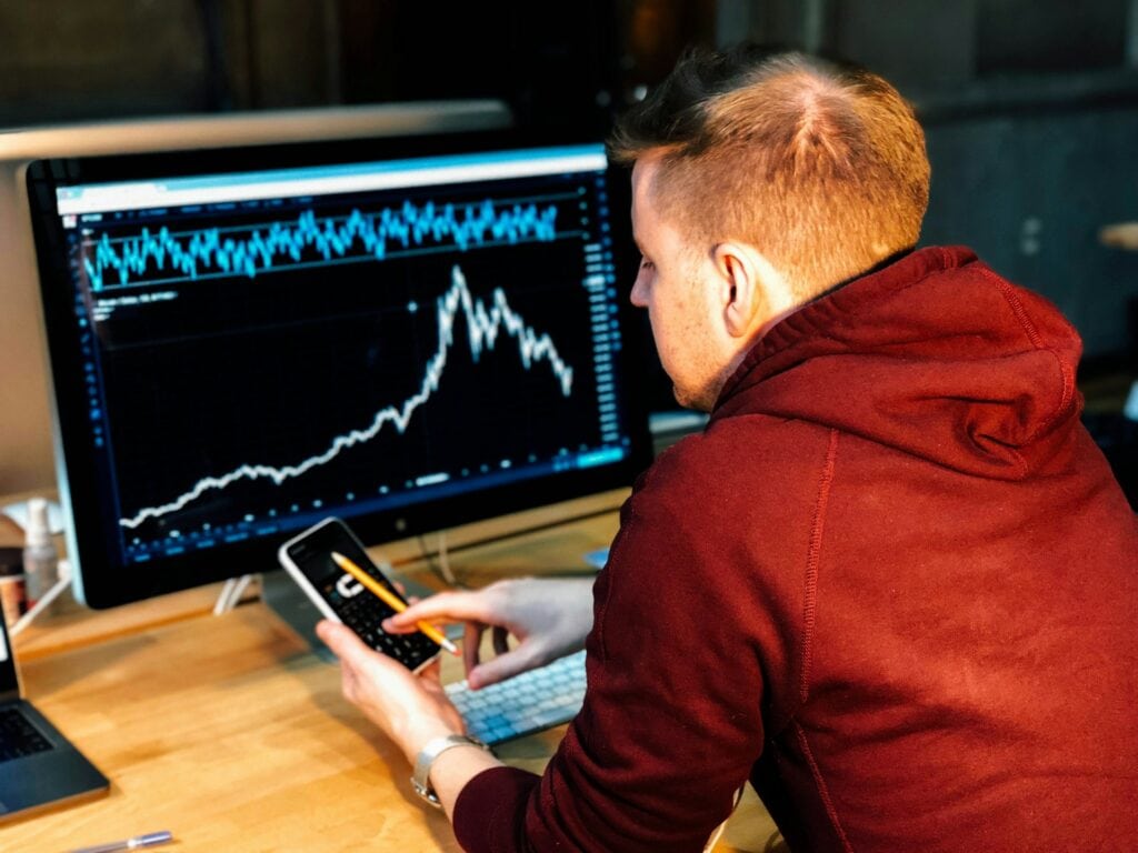man holds phone while studying computer screen.