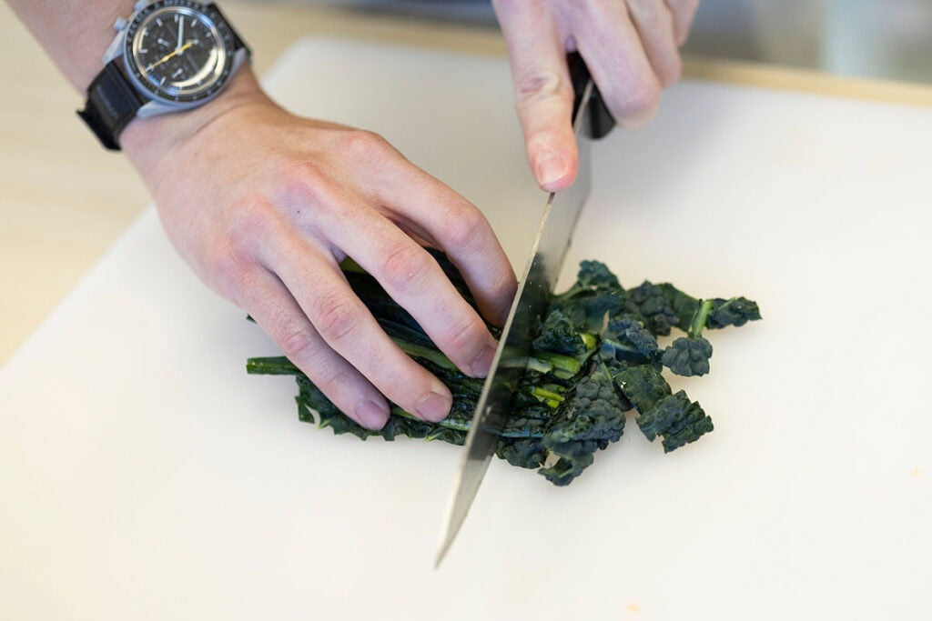 Hands cutting kale on a cutting board.