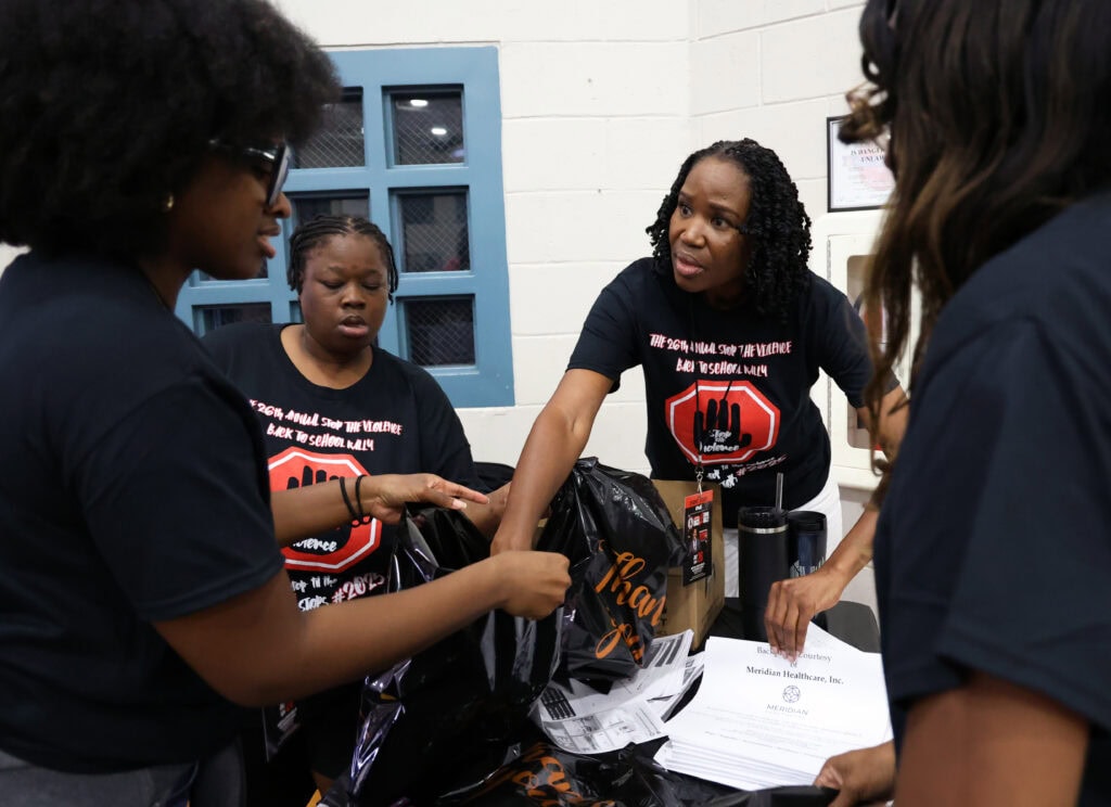 Joyce Randan (center) works with Bridget Anderson (left) and Kristen Cooper (right) to stuff informational flyers into goodie bags for incoming families during the Stop the Violence Back to School Rally.