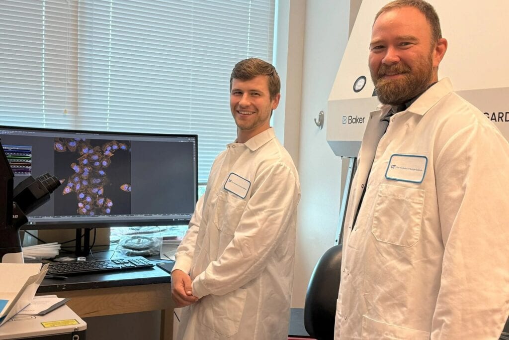 Skyler Briggs, a graduate student at The Wertheim UF Scripps Institute, shows a microscopic image of lung cells infected with West Nile virus, with Dr. James Burke (right).