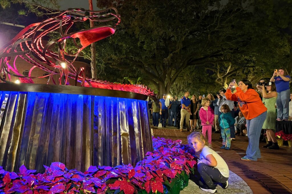 A young girl kneels beside poinsettias encircling the Holiday Gator. Photo by Megan V. Winslow