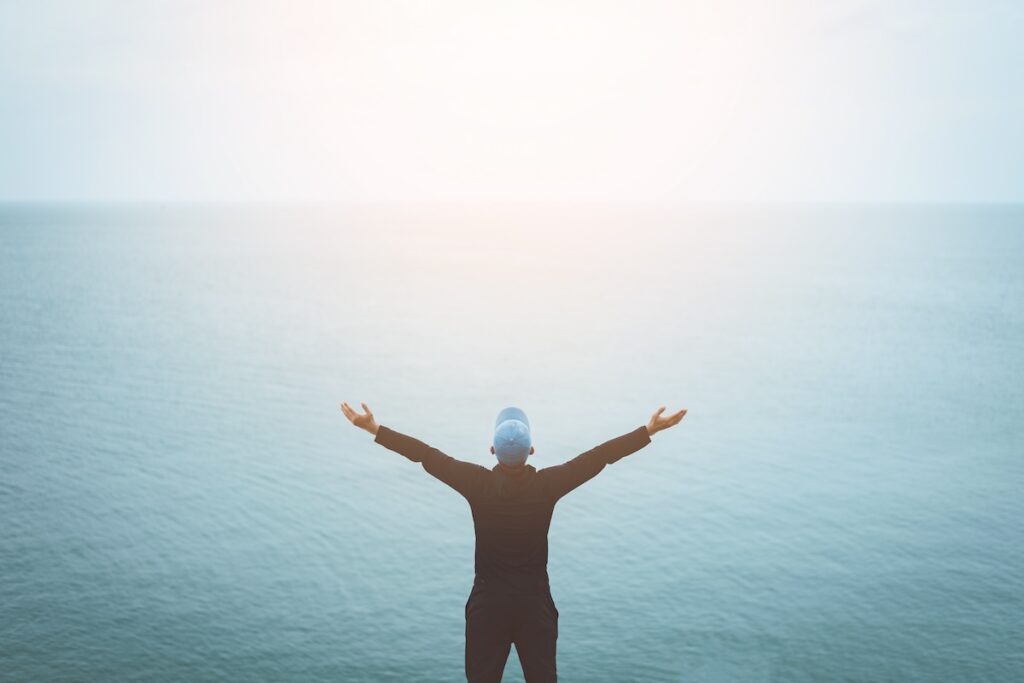 Person with their hands raised facing the ocean