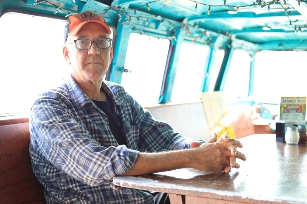 Satchel Raye, owner of Satchel's Pizza, sits at a table inside the well-known van outside his business.