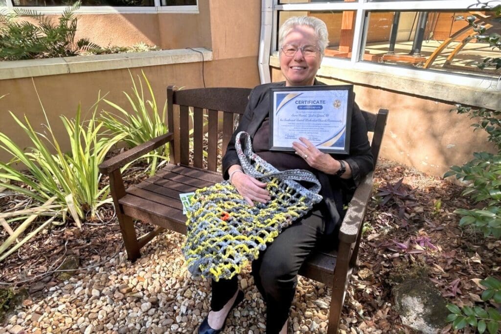 Sara Nussel, chief organizer of the effort, sits at the bench at Temple Shir Shalom, with the handbag she made out of plastic on her lap and her award certificate in hand. Photo by Ronnie Lovler (1)