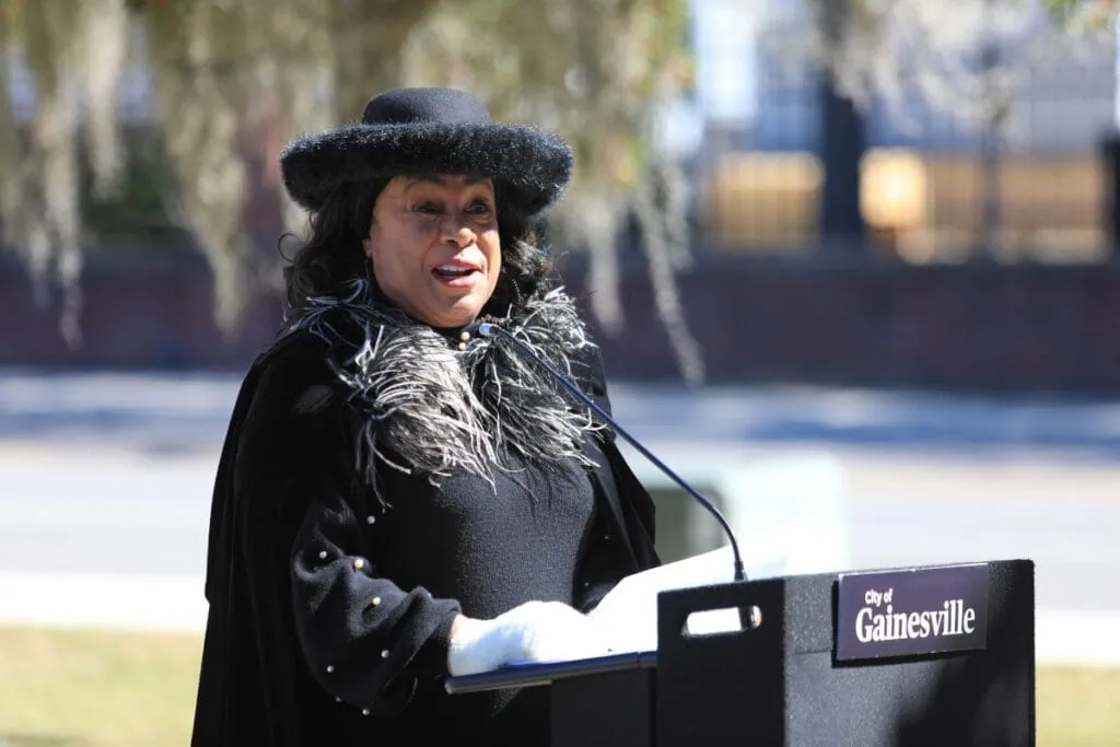 Bonnie Burgess, president of the Rosa Parks Quiet Courage Committee, speaks outside from behind a podium.