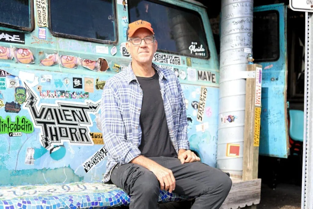 Satchel Raye sits on a bench beside the VW minivan parked outside his restaurant.