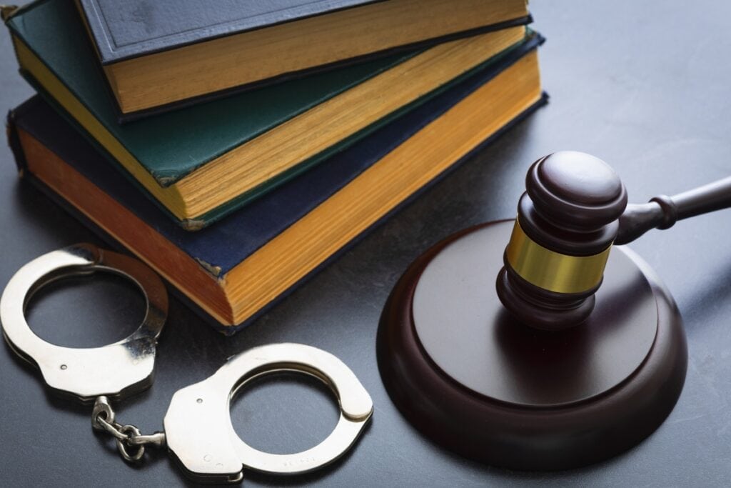 A photo of handcuffs with a judge's gavel and books.