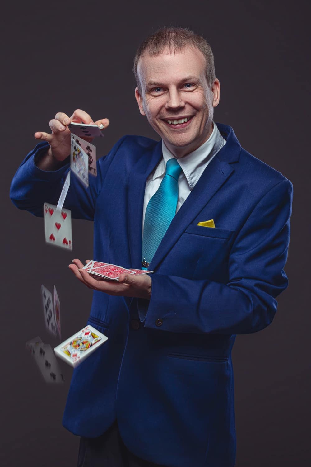 A man in a blue suit is holding cards and playing cards.