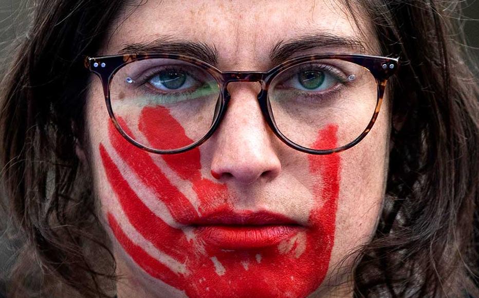 A woman wears red face paint depicting a hand during a pro women's rights protest.