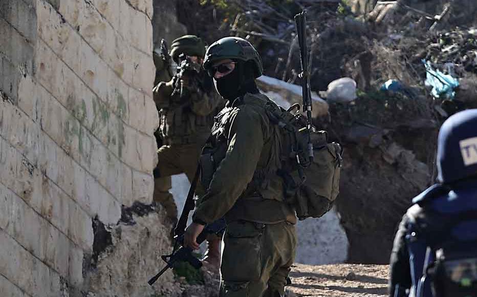 An Israeli soldier takes aim from behind a wall as journalists cover their patrol in the Jenin refugee camp, in the occupied West Bank on November 29, 2023, during an ongoing military operation in the camp.