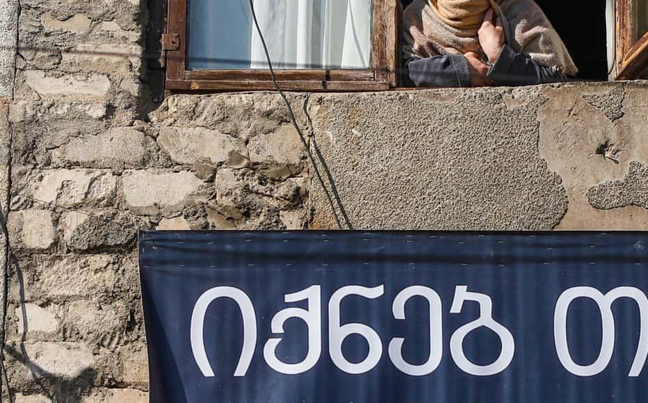 Diana Davlianidze, 49, looks out from the window by the banner, “Maybe at least you can be helped.” On January 16, Zurab Kiria, 52, an IDP, killed himself. According to his neighbours, his last words were, “Maybe at least you can be helped.” 