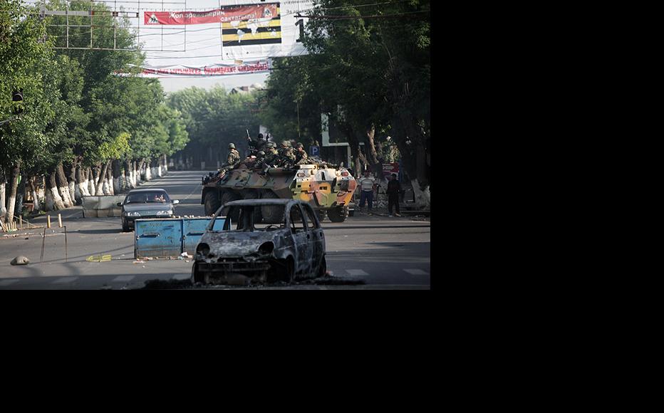 Kyrgyz security forces drive past a burnt-out car blocking a road in Osh. (Photo: Inga Sikorskaya)