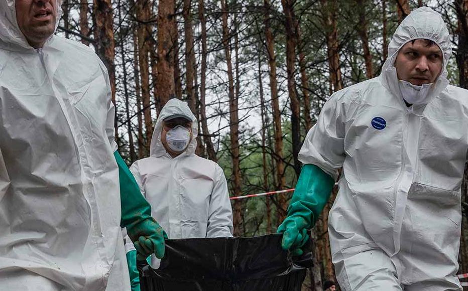 Employees of Ukraine’s state emergency service carry a body bag in the pine forest in the outskirts of the retaken town of Izyum. Ukrainian authorities discovered a mass burial site with hundreds of graves.