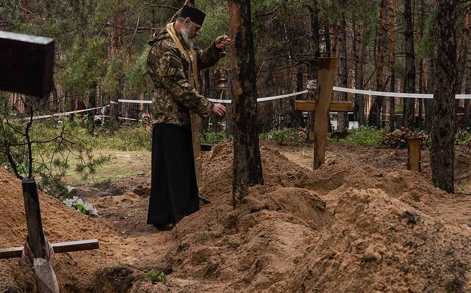 Priest Yuriy Potykun conducts a memorial service at the mass burial site in the forest on the outskirts of Izyum.