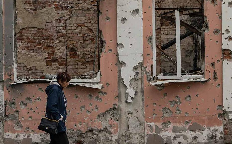 A woman walks in front of the skeleton of a building in central Izyum. Hardly a building in the town is left undamaged.