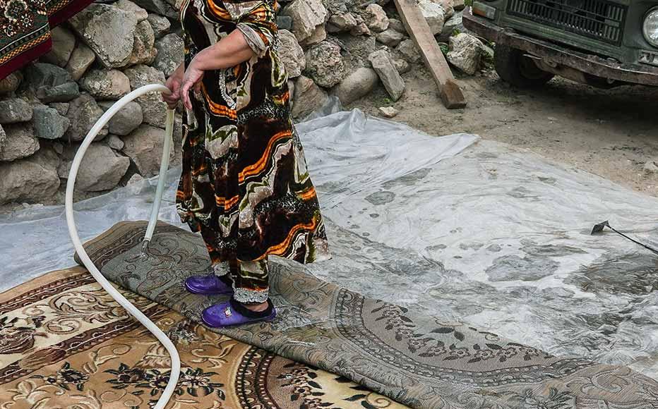 A woman washes carpets in the street by her house. Carpets are central to Tajik houses and are regularly beaten and scrubbed.