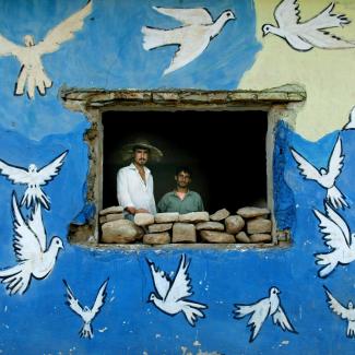 Northern Iraqi Kurds Hendrin Usman (L) and Ubeid Hasen look out a window of their house adorned with doves June 16, 2003 in a village near Erbil, Iraq.