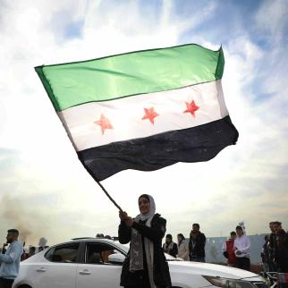 A woman waves the flag of the Syrian rebels as people gather to celebrate the fall of the government, in Umayyad Square on December 8, 2024 in Damascus, Syria. Rebel forces in Syria claimed that they had retaken the capital from longtime ruler Bashar al-Assad, who was reported to have fled the country. 