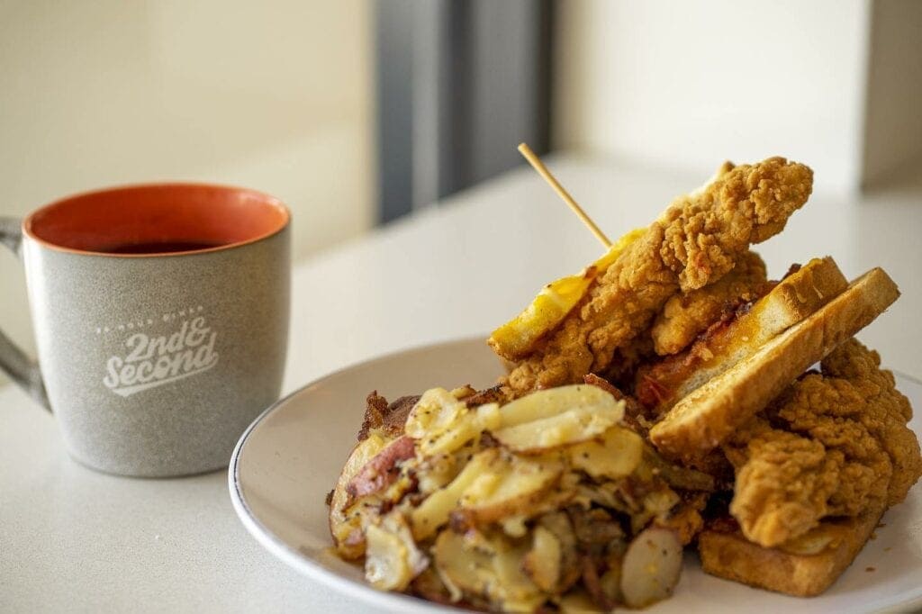 Fried chicken sandwich next to a coffee mug with a side of hash browns 