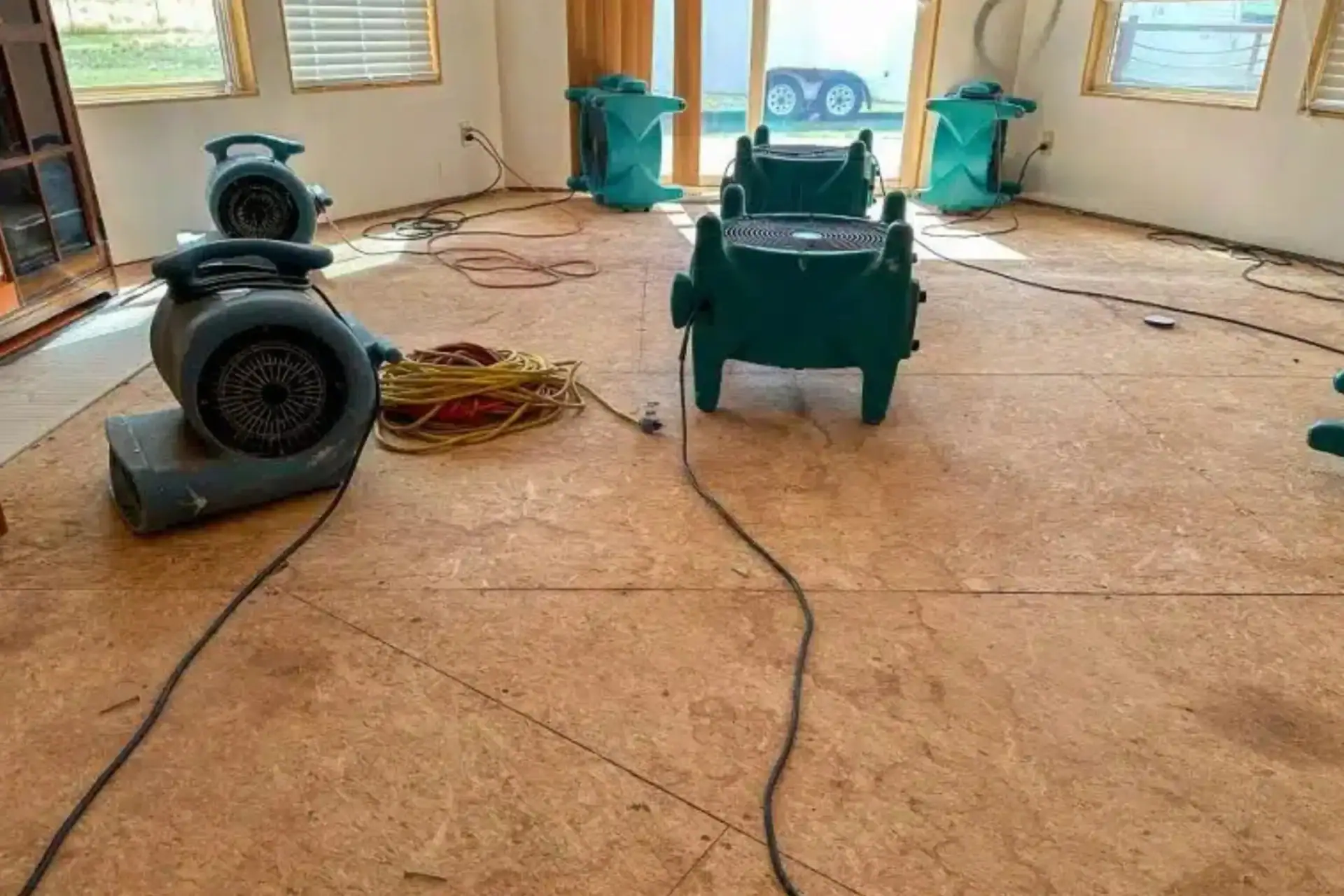 A row of industrial-strength air movers and a large dehumidifier drying out a hardwood floor in a living room