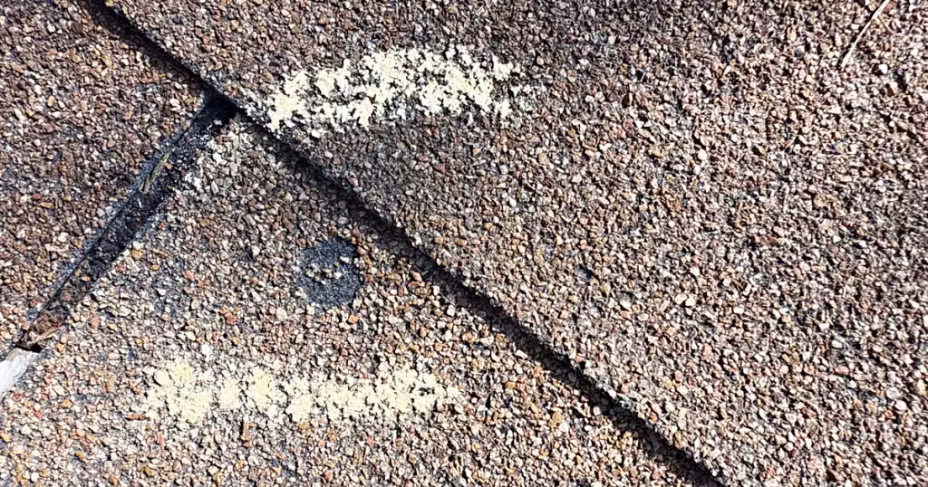Roofing contractor inspecting hail damage impact marks on residential roof shingles in McKinney, TX