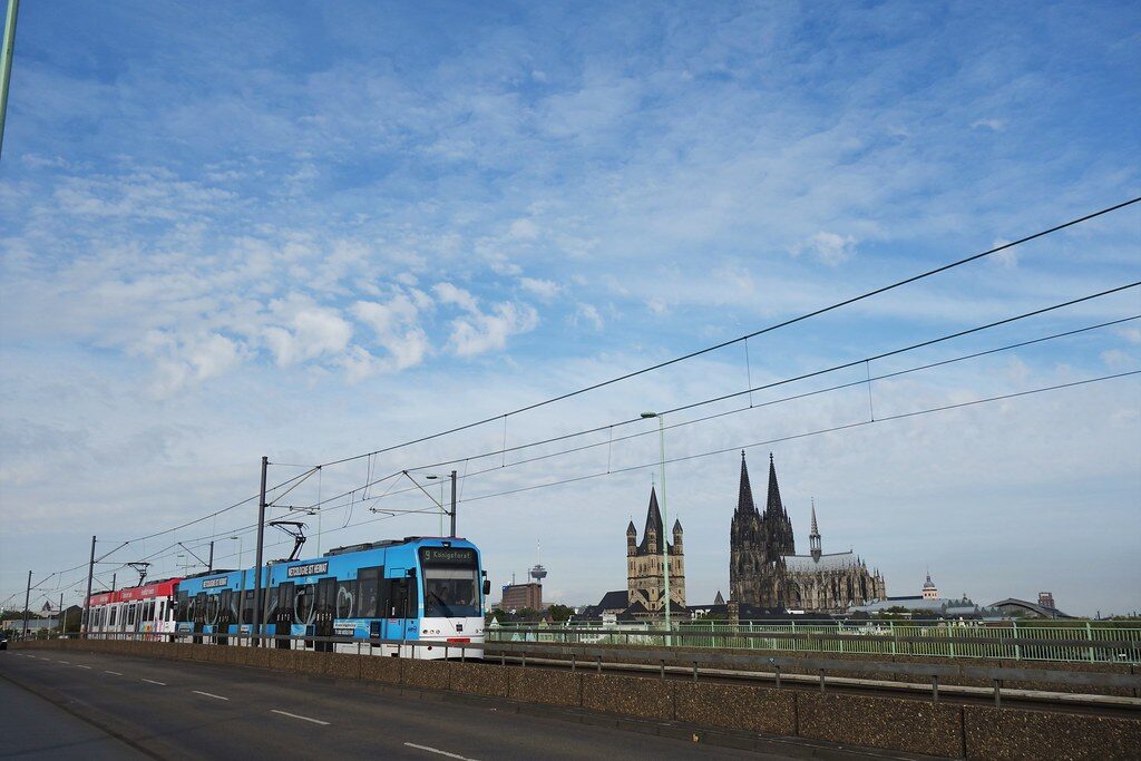 Moderne Stadtbahn fährt an Kölner Dom und Kirche vorbei.