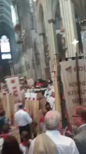 Farbenfrohe Prozession mit Fahnen der Sebastianus & Afra Schützenbruderschaft im Kölner Dom, festliche Stimmung, Gläubige in traditioneller Tracht, historische Schützenfahnen, religiöse Feierlichkeit, kirchliches Ereignis, traditionelles Brauchtum in Köln.
