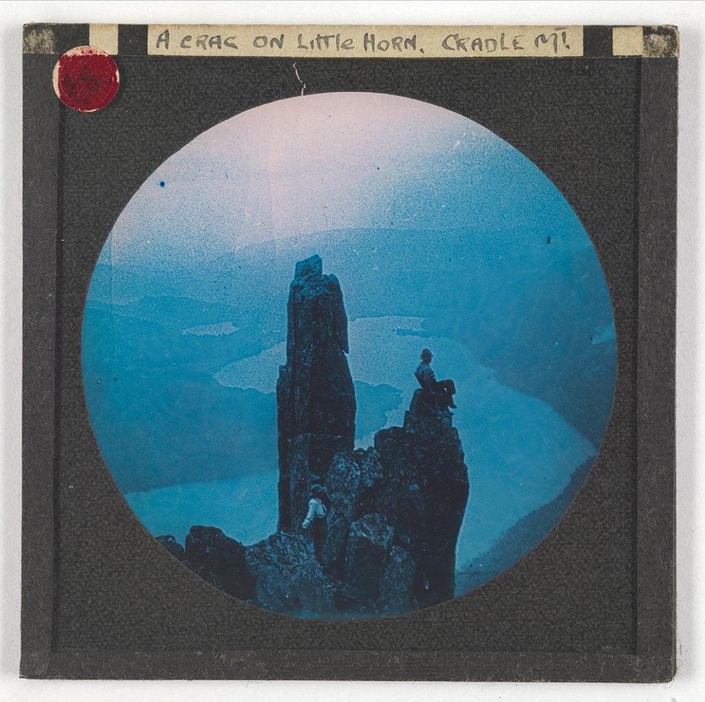 Photograph - 'A Crag on Little Horn, Cradle Mt.' (woman standing, man seated on high rocks) (circle frame) [Lantern Slide - blue tone ] [Box 4]
