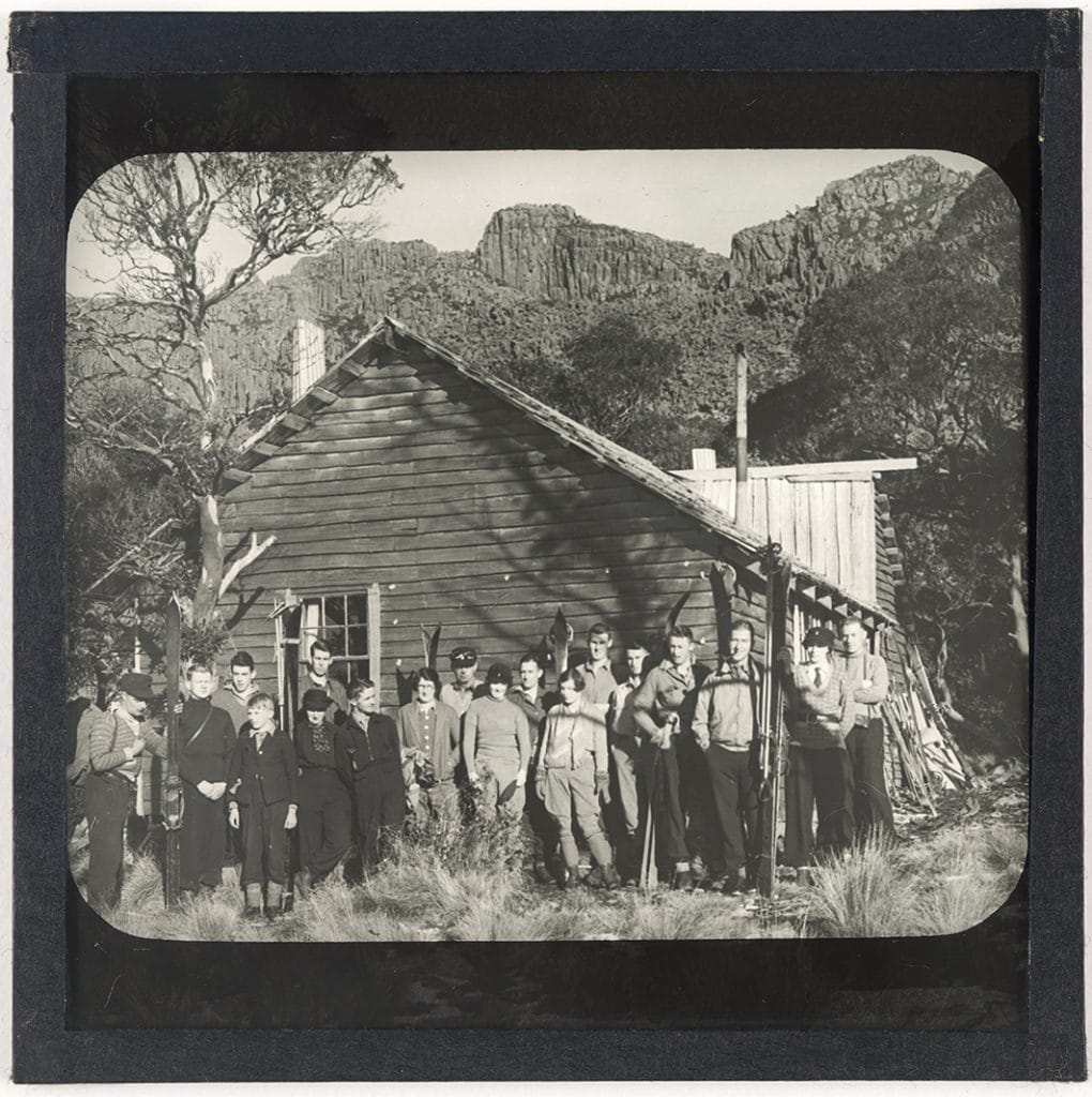 Photograph - Group of eighteen people posing for photograph outside wooden hut [Legges Tor ?] / Frederick Smithies [Lantern Slide] [Box 1]