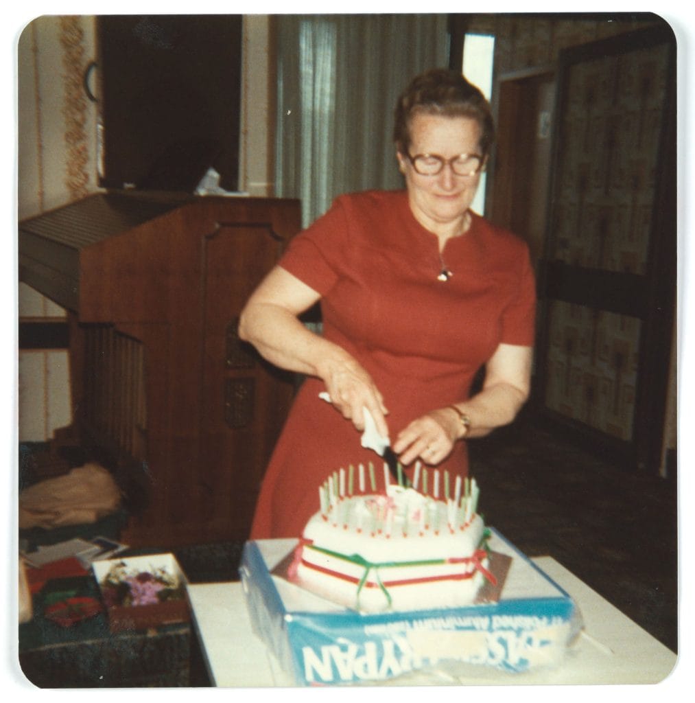 Woman in red dress cuts a cake with candles and red and green ribbon